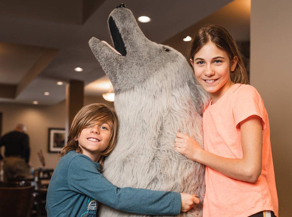 Two kids posing with the Gray Wolf Inn & Suites mascot "Caldera"