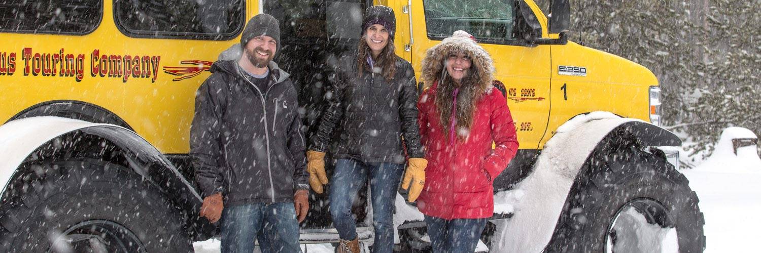 Man and two women standing outside winter snowcoach tour bus