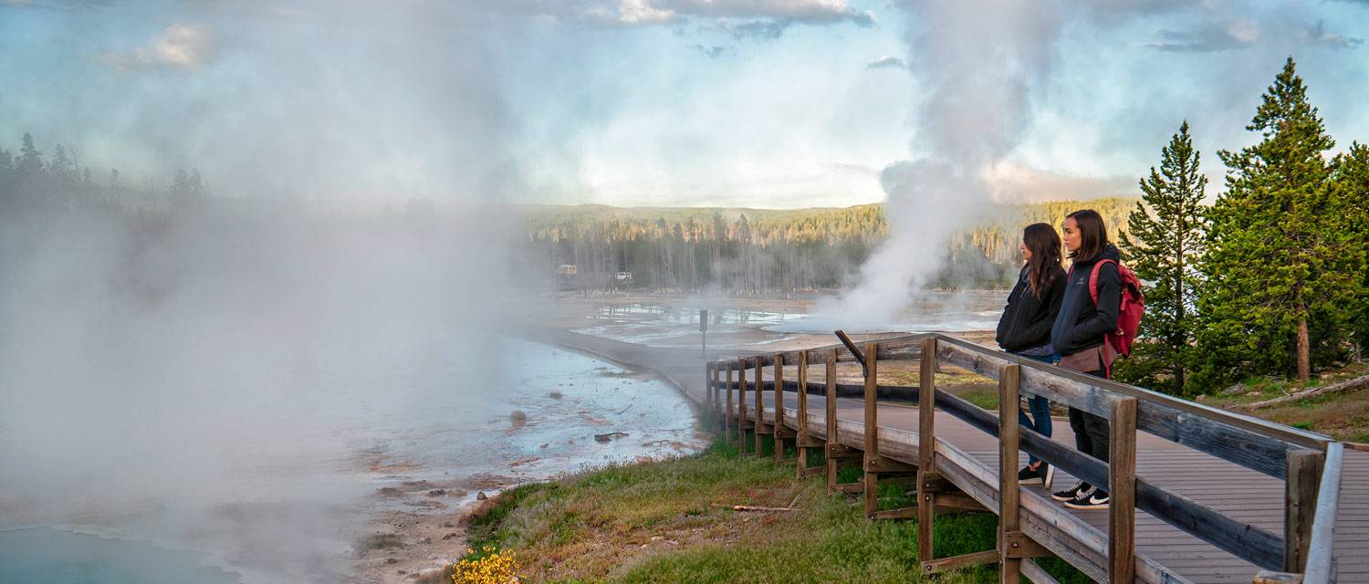 Two Yellowstone visitors looking at hot springs from the boardwalk