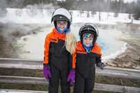 Two kids posing by a thermal feature on a Yellowstone snowmobile tour