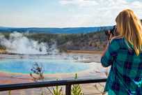 A summer bus tour passenger stops to take a photo of Grand Prismatic Springs